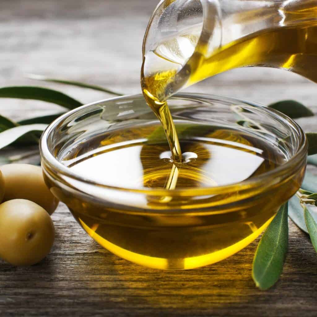 olive oil being poured from a bottle to a small bowl that is sitting on the table.