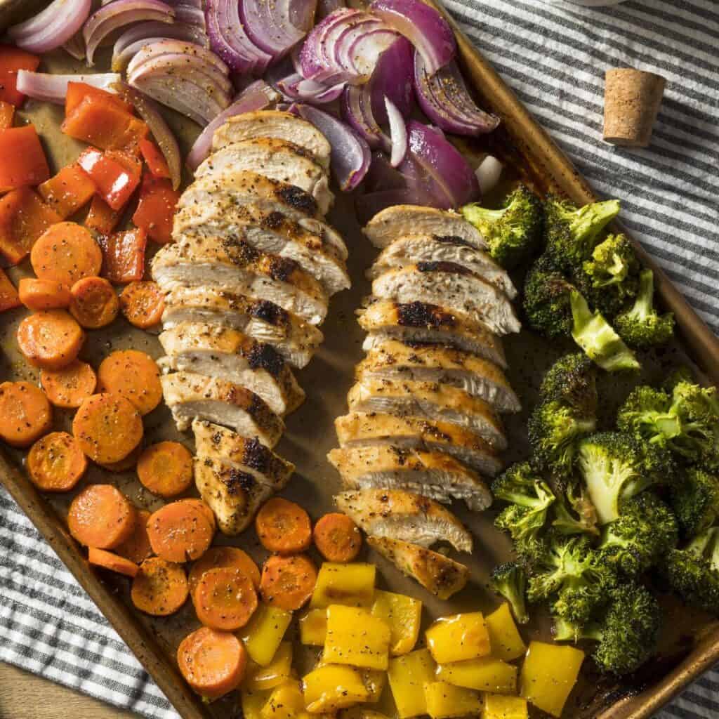 chicken, broccoli, red onion, carrots, yellow and red peppers on a cookie sheet