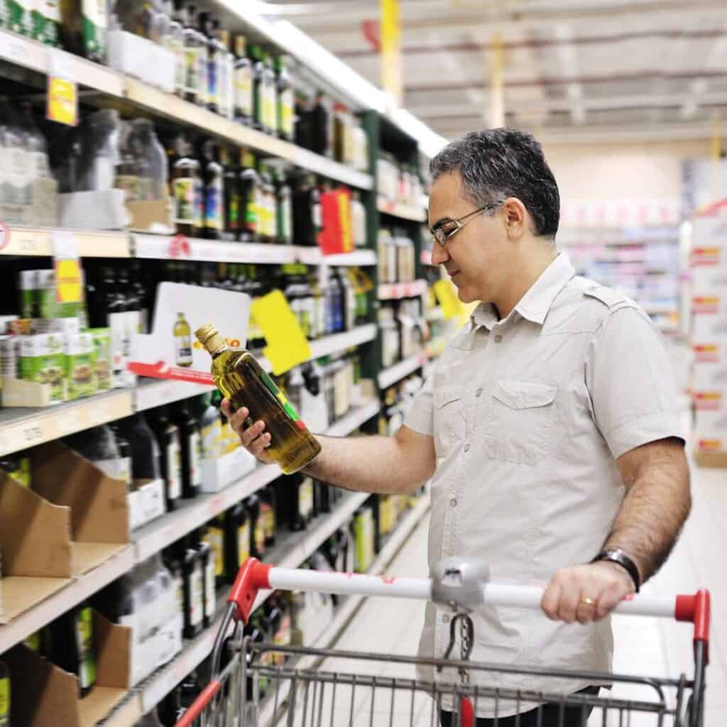 man in a grocery store looking at a bottle of olive oil