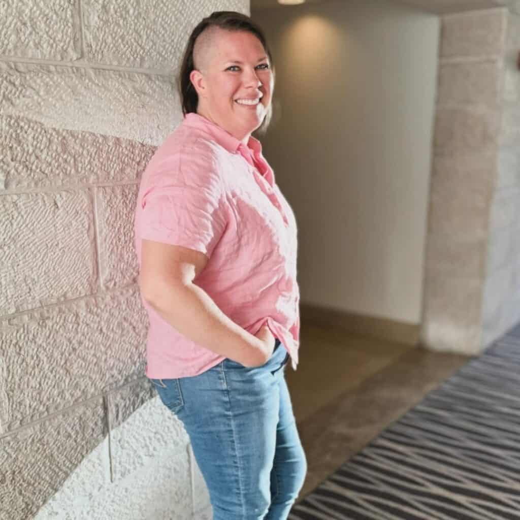 Kimberly in a pink linen shirt and jeans leaning against a tan limestone wall