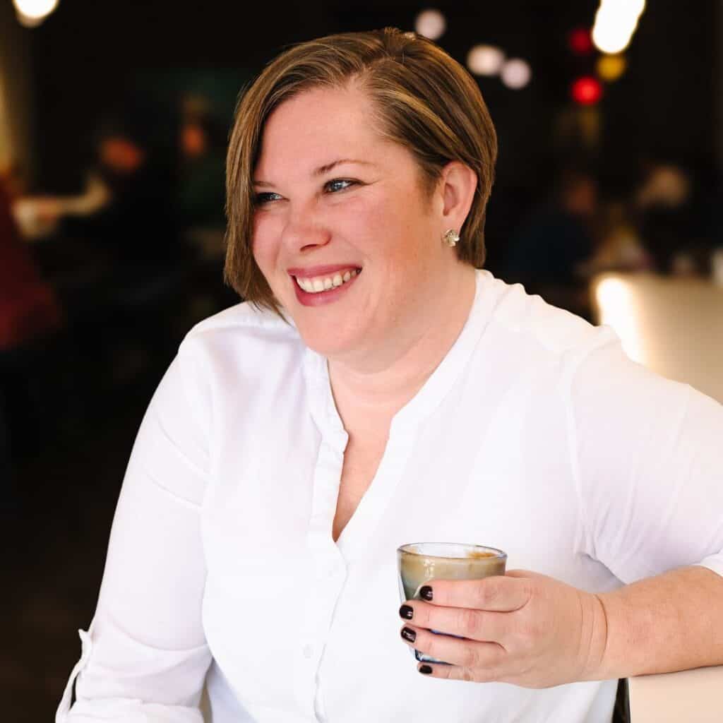 Kimberly holding a cup of coffee in a white blouse at a bar in a cafe